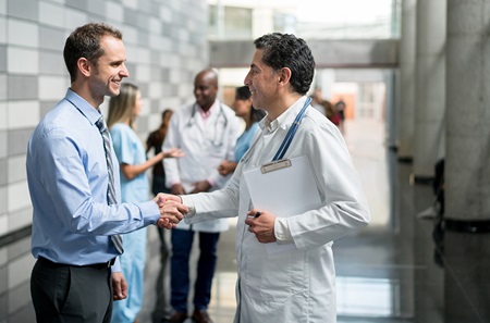 Senior and junior clinicians shake hands at a meeting.